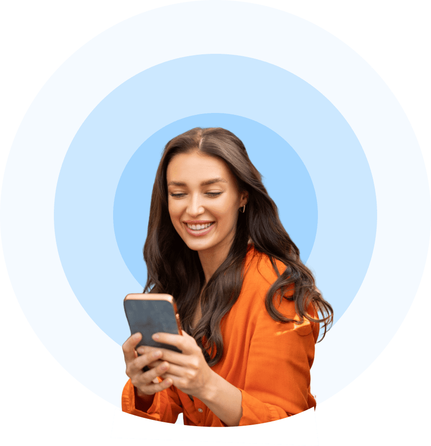 A woman in an orange sweater smiling while using her smartphone.